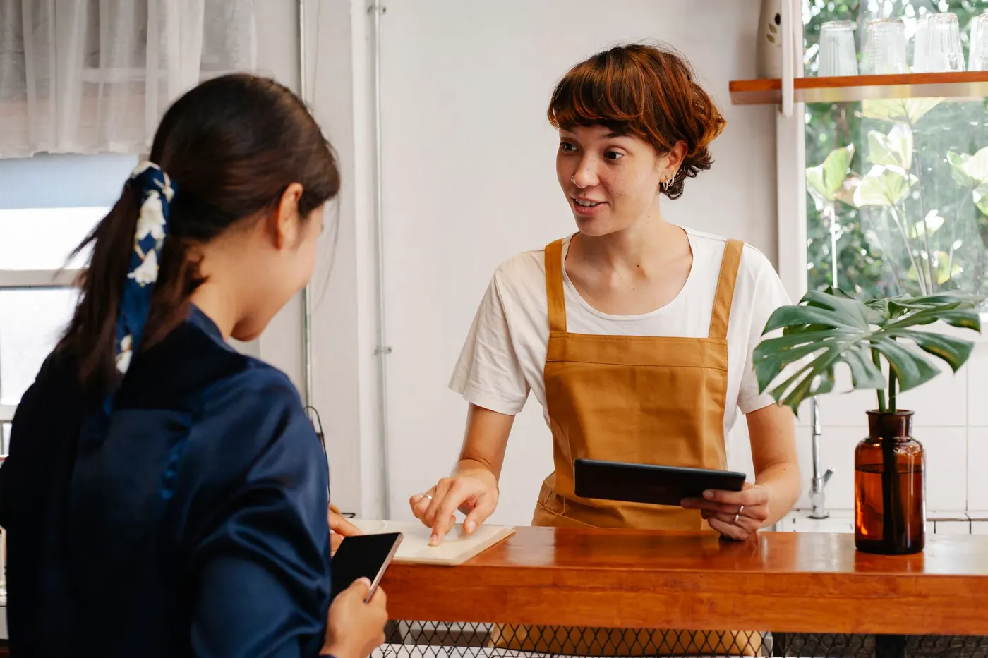 Mitarbeiterin mit Tablet an der Theke eines Cafés im Gespräch mit einer Kundin